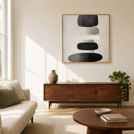 Minimalist abstract canvas of balanced stacked stones in black, grey, and ivory, framed in wood above a walnut sideboard in a calm modern living room.