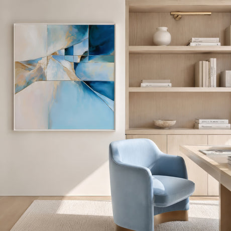 Abstract blue and gold geometric wall art in white frame, hung in a sunlit small office with pale blue chair.