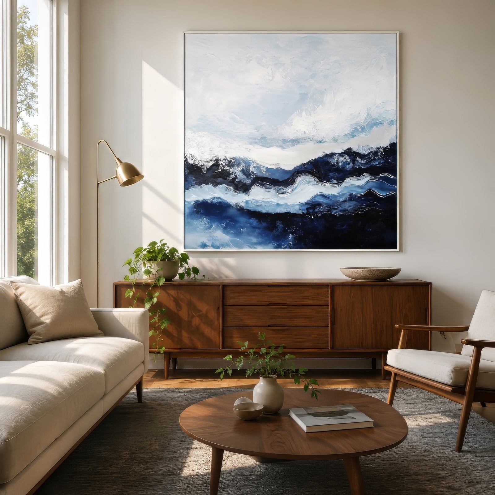 Abstract navy and white lake landscape print in white frame above linen sofa in a calm mid-century living room.