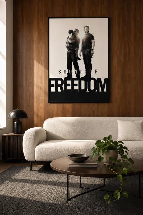 Sound of Freedom black and white movie poster in a framed print, hung on a wood-panel wall above a cream boucle sofa in a warm monochrome living room.