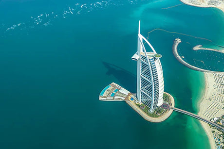 Aerial view of the iconic Burj Al Arab tower, artificial island, and surrounding oceanic landforms in Dubai.