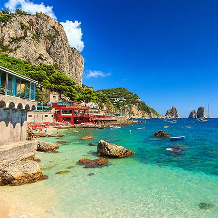 Capri wall art featuring vibrant seaside village with turquoise waters, rugged cliffs, and boats along the shoreline — Capri Wall Art Collection for Mediterranean coastal decor.
