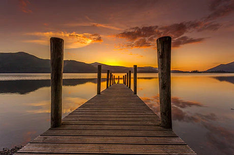 Dusk sunset at Cumbria with water reflection, pier, dock, and boardwalk under a fiery afterglow sky.