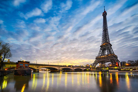 Dusk view of iconic French landmark, a tower and bridge architecture, under a blue sky with clouds reflected