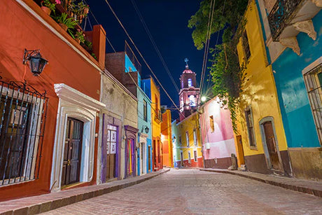 Evening scene of a cobblestone alley in Guanajuato town with vibrant wall art, captured in stock photography.