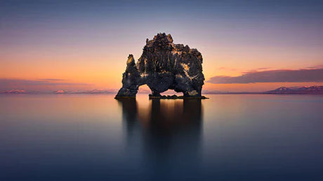 Icelandic coastal landforms at dusk, featuring blue ocean, rock formations and horizon