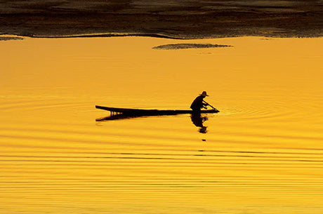 Silhouette of a boat and paddler on a serene lake in Laos, reflected beautifully in the water.
