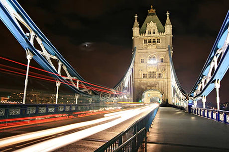 Nighttime view of iconic London suspension bridge with city's metropolitan area backdrop.
