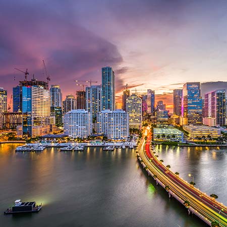 Miami skyline at sunset with illuminated high-rises and vibrant bridge lights reflecting on Biscayne Bay – modern cityscape wall art for urban home or office décor.