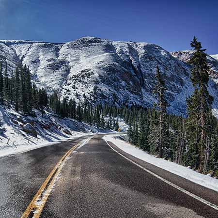 Snow-covered Pikes Peak highway winding through alpine forest and rocky mountains in Colorado – dramatic winter landscape wall art for rustic home or office décor.