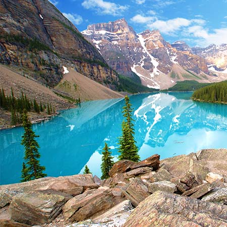 Turquoise alpine lake reflecting snow-capped Rocky Mountains with pine trees and rugged cliffs – stunning landscape wall art for mountain-themed home décor.