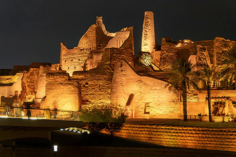 Nighttime view of historic Saudi Arabian landmark with palm trees and landscape lighting