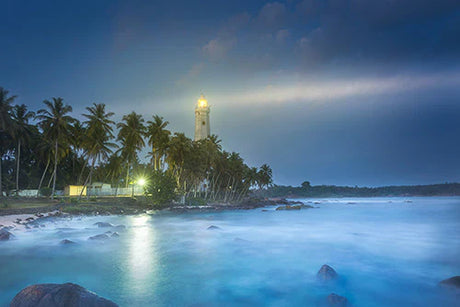 Blue lighthouse tower on Sri Lanka's coastal shoreline with beacon overlooking ocean and beach