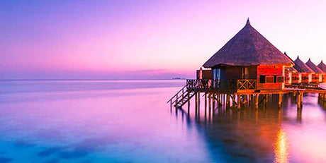 Dusk view of a resort with beach huts, pier, on Tahiti's coastal landforms overlooking the ocean
