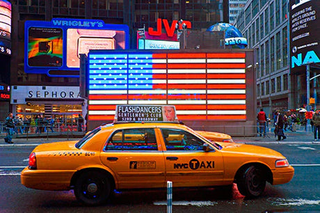 Full-size taxi cab in Times Square with vibrant advertising logos and automotive lighting