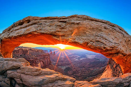 Sunrise over a natural arch and geological formations in Utah's wilderness terrain