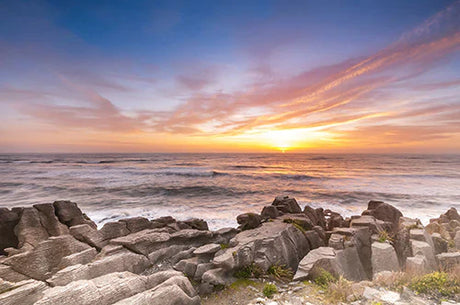 West Coast Collection wall art featuring a stunning sunrise with red sky, sea, rocks, and dusky horizon.