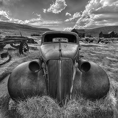 Monochrome photography of a classic vintage car with detailed hood, grille, and fender.