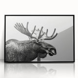Framed wall art featuring a moose and elk design, showcasing wildlife in a natural habitat. The piece is presented in a sleek black frame, ideal for enhancing rustic or nature-themed decor.