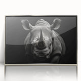 Framed wall art featuring a striking front view of a rhinoceros, showcasing intricate details and a sleek silver-acrylic finish, perfect for wildlife enthusiasts.