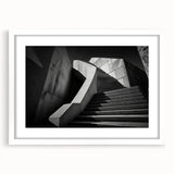 Abstract art print of a spiraling staircase in monochrome, framed with a white mat.