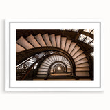 Abstract art print of a spiral staircase in muted gray and white, framed with a white mat.