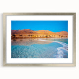 Textured art depicting the Dead Sea in muted blue and beige tones, framed with a silver mat, suitable for bedroom decor.