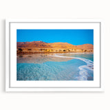 Abstract art print of the Dead Sea in muted blue and beige tones, framed with a white mat, ideal for dining room decor.
