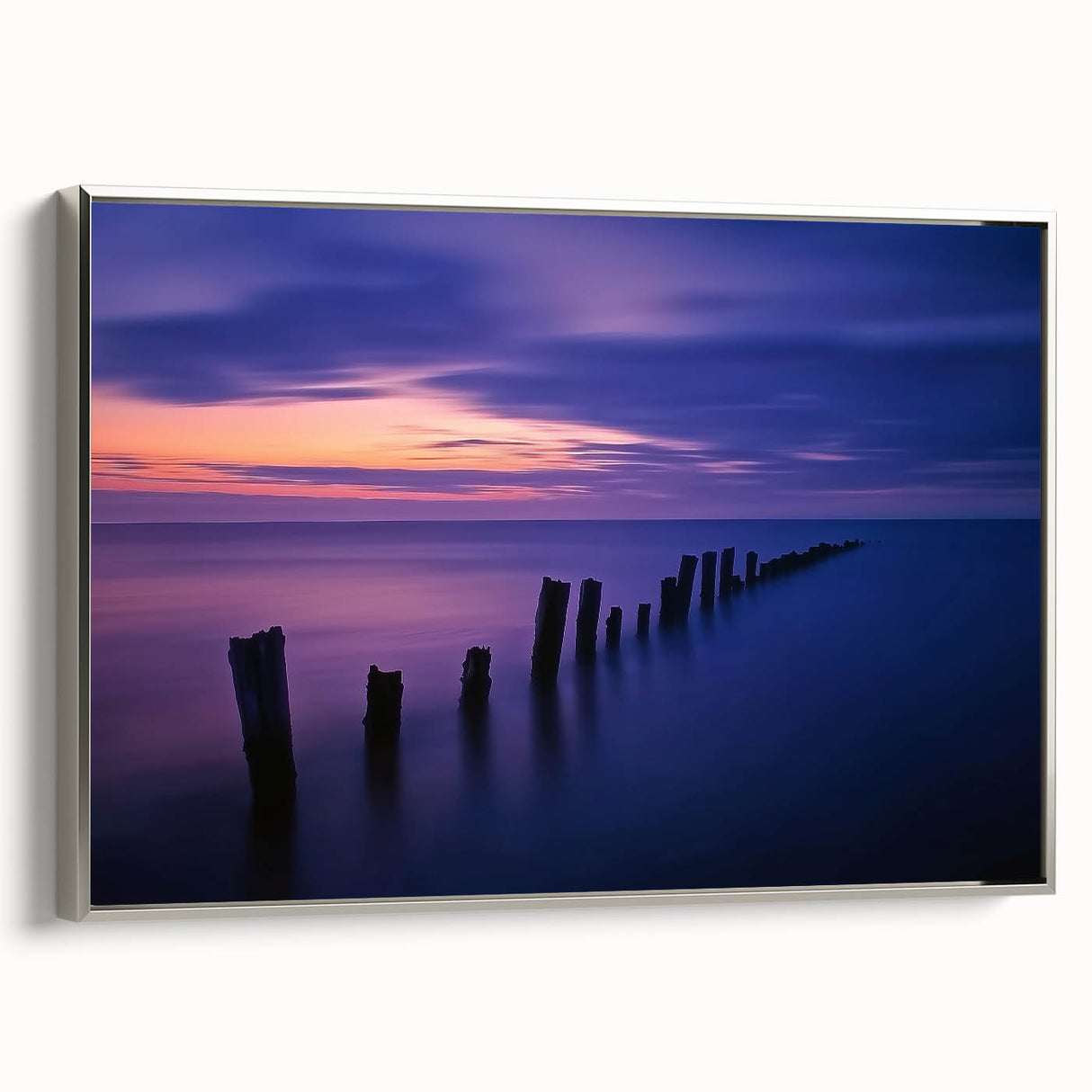 Framed canvas print depicting a serene beach landscape with soft waves and a vibrant sunset, showcasing a silver frame from a side view, perfect for coastal decor.