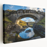 Stretched canvas artwork of a serene landscape featuring a bridge over a tranquil river, with lush greenery and soft clouds in the background, ideal for home decor.