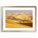 Framed desert landscape artwork featuring a serene sunset with warm tones, encased in a sleek silver frame with a white mat, ideal for home decor.