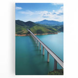 Vibrant landscape canvas featuring a serene bridge over a flowing river, surrounded by lush greenery and a clear blue sky, ideal for home decor.