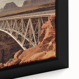 Close-up of a framed landscape canvas print showcasing a serene bridge over a tranquil river, surrounded by lush green foliage and vibrant colors, perfect for home decor.