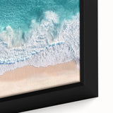 Framed landscape canvas depicting a serene beach scene with golden sand and turquoise waves, showcasing vibrant colors and intricate details for a calming decor accent.