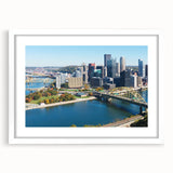 Abstract art print of Pittsburgh skyline in muted gray and blue tones on a framed white mat, suitable for dining room decor.