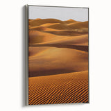 Framed canvas artwork showcasing a serene desert landscape of dunes, featuring soft beige and golden hues, elegantly displayed with a silver frame for a modern touch.