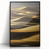 Framed acrylic artwork showcasing a serene landscape of rolling dunes in soft beige and golden hues, set in a sleek black frame, ideal for modern home decor.