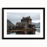 Framed landscape artwork showcasing a majestic castle surrounded by lush greenery, displayed in a sleek black frame with a white mat, ideal for home decor.