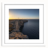 Framed landscape artwork of rugged cliffs and serene ocean waves, displayed in a modern white mat, perfect for adding a touch of nature-inspired decor to any room.