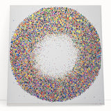 Abstract canvas art featuring colorful splatters in vibrant hues of blue, pink, and yellow, leaning against a neutral wall, perfect for modern decor. This striking piece adds a dynamic touch to any interior space, enhancing artistic expression.