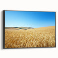 Framed canvas artwork depicting a serene countryside landscape featuring rolling hills, lush greenery, and vibrant blue skies, showcased in a sleek black frame.