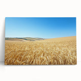 Stretched canvas artwork depicting a serene countryside landscape with rolling hills and vibrant greenery, leaning against a textured wall, perfect for home decor.