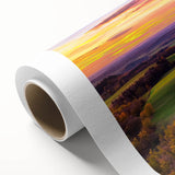 Rolled canvas displaying a serene countryside landscape with vibrant green fields and a clear blue sky, elegantly packaged in a protective cardboard tube.