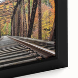 Close-up of a framed landscape canvas artwork depicting a serene bridge over a tranquil river, surrounded by lush greenery, perfect for home decor and nature lovers.
