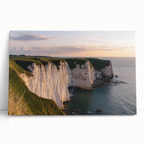 Stretched canvas artwork showcasing a dramatic landscape of cliffs under a vibrant sunset, leaning against a wall, perfect for home decor and visual impact.