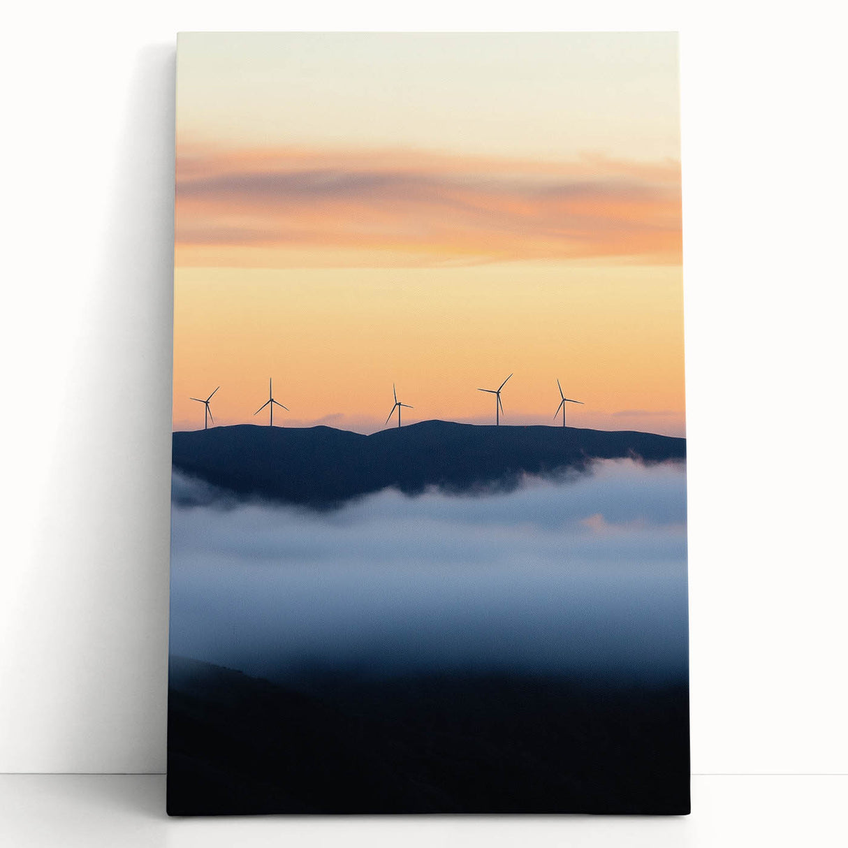 Stretched canvas artwork depicting a serene countryside landscape with lush green fields and a vibrant sky, leaning against a rustic wall, ideal for home decor.