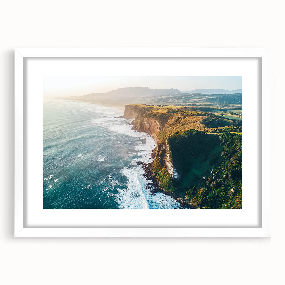 Framed landscape artwork depicting dramatic cliffs against a vibrant sunset, featuring a white mat and sleek black frame, ideal for home decor.