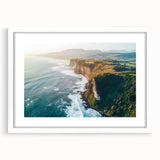 Framed landscape artwork depicting dramatic cliffs against a vibrant sunset, featuring a white mat and sleek black frame, ideal for home decor.