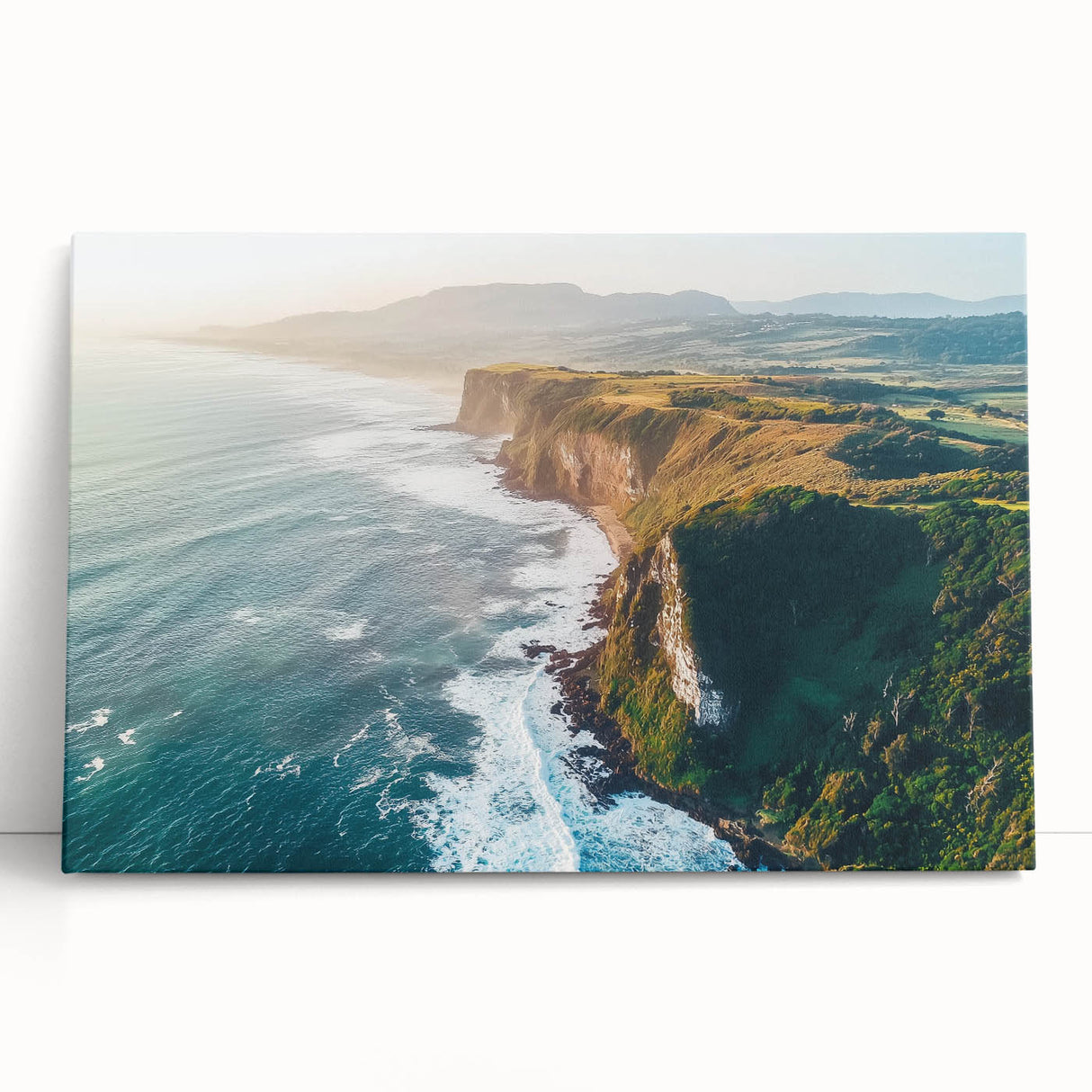 Stretched canvas art depicting a vibrant landscape with dramatic cliffs and lush greenery, showcasing natural beauty in a modern home setting.