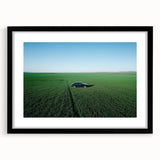 Black-framed landscape art print showcasing a serene countryside scene with vibrant greens and rolling hills, enhanced by a white mat, perfect for home decor.
